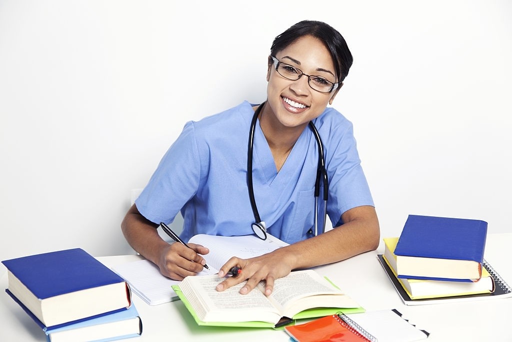 Beautiful mixed race woman with black hair wearing a blue medical scrub uniform along with a stethoscope while studying