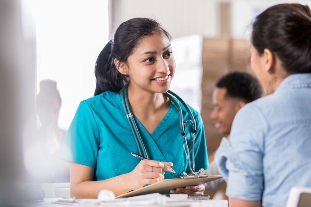 Young female Hispanic volunteer healthcare professional talks with female patient about her medical history